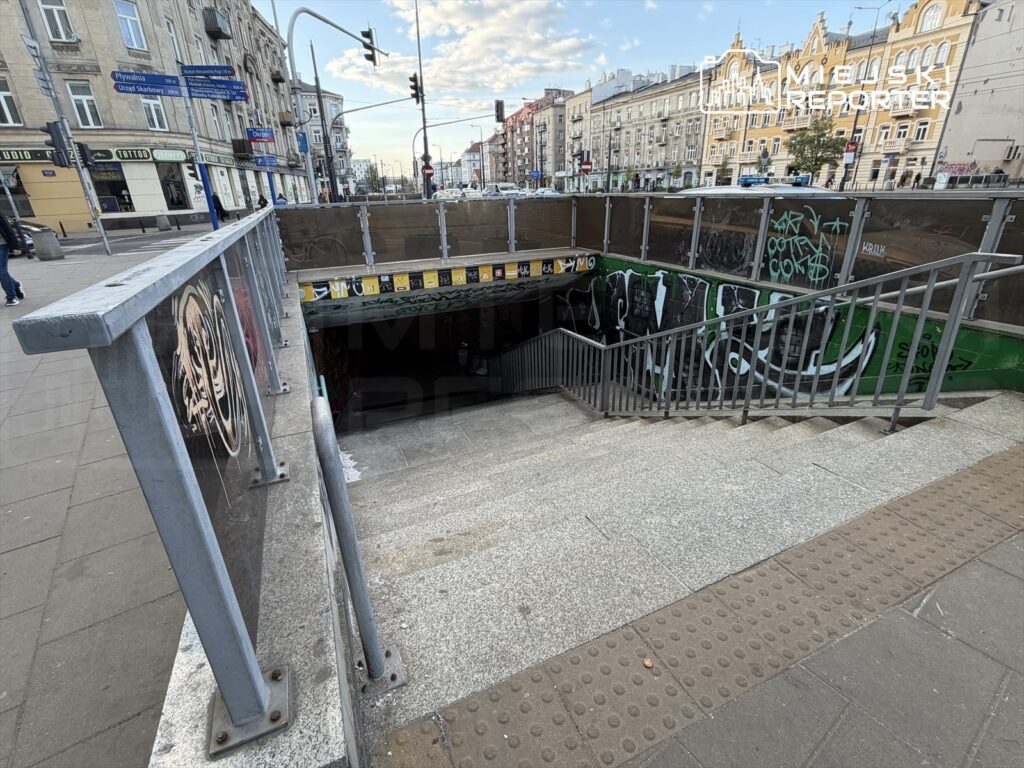 Schody prowadzące do podziemnego przejścia, z metalową barierką i graffiti na ścianach, w miejskim otoczeniu.