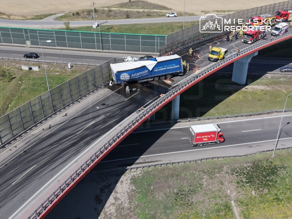 Cysterna przewożąca ładunek stoi na moście, a służby ratunkowe pracują nad usunięciem skutków wypadku.