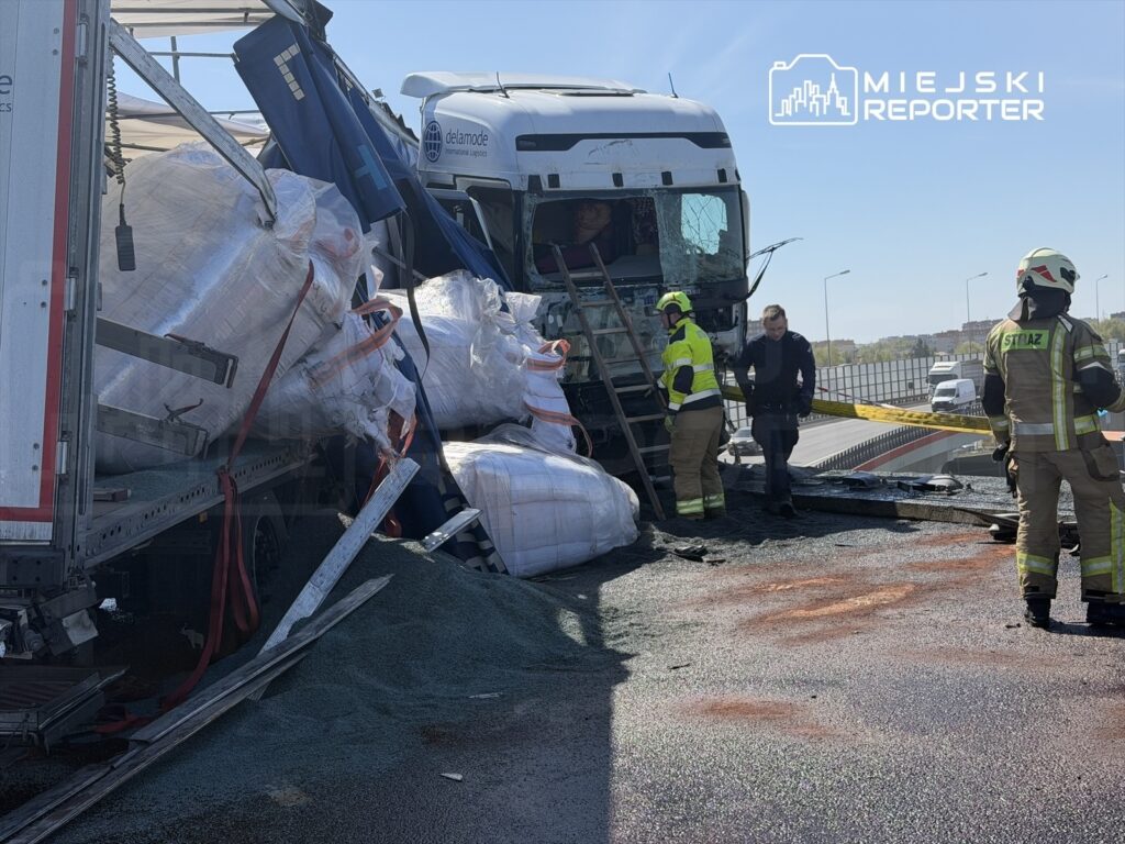 Czterech ratowników w mundurach pracuje przy przewróconej ciężarówce, z której wysypał się ładunek.
