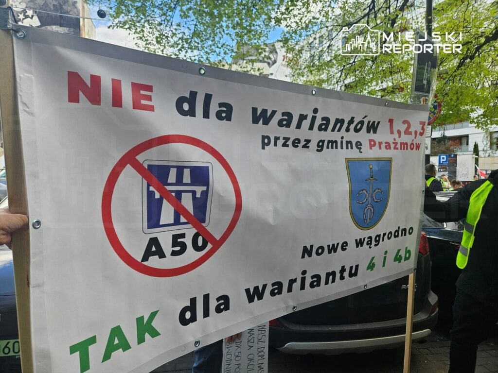 Manifestujący trzymają transparent z napisem "NIE dla wariantów 1,2,3 przez gminę Prazmów" oraz symbolem zakazu.