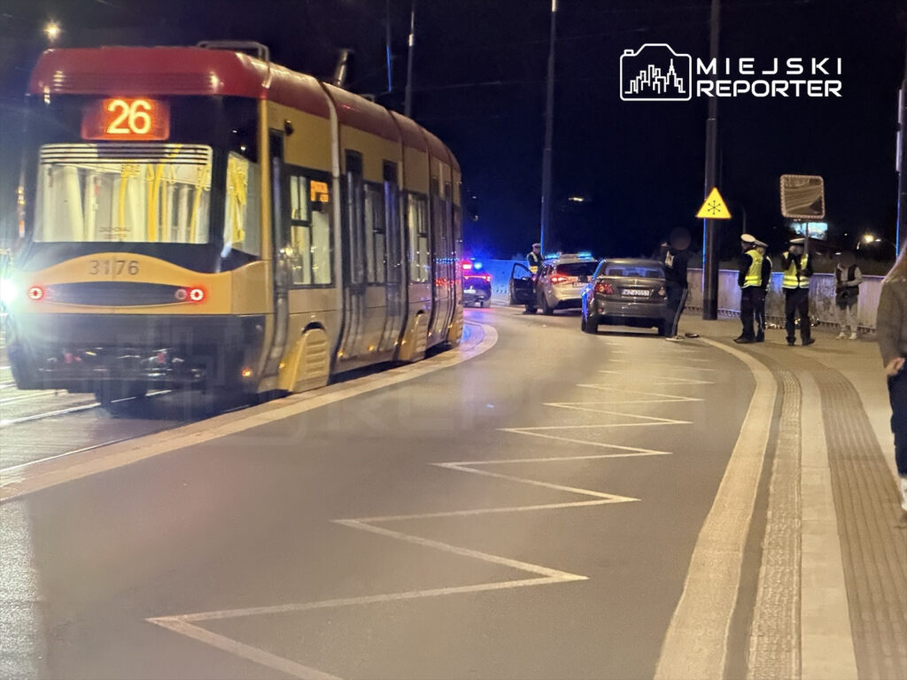 Tramwaj linii 26 zatrzymany na przystanku, obok policyjne samochody i funkcjonariusze kontrolujący sytuację.