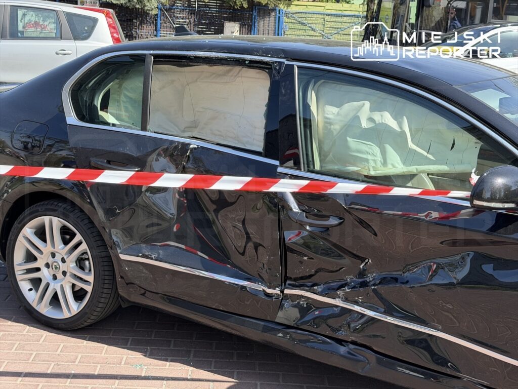 Czarny samochód osobowy z uszkodzoną lewą stroną, zabezpieczony taśmą ostrzegawczą, zaparkowany na chodniku.