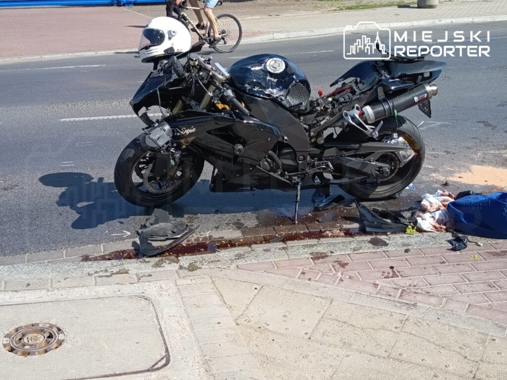 Motocykl sportowy leży na jezdni, obok widoczne ślady płynów oraz uszkodzone elementy pojazdu.