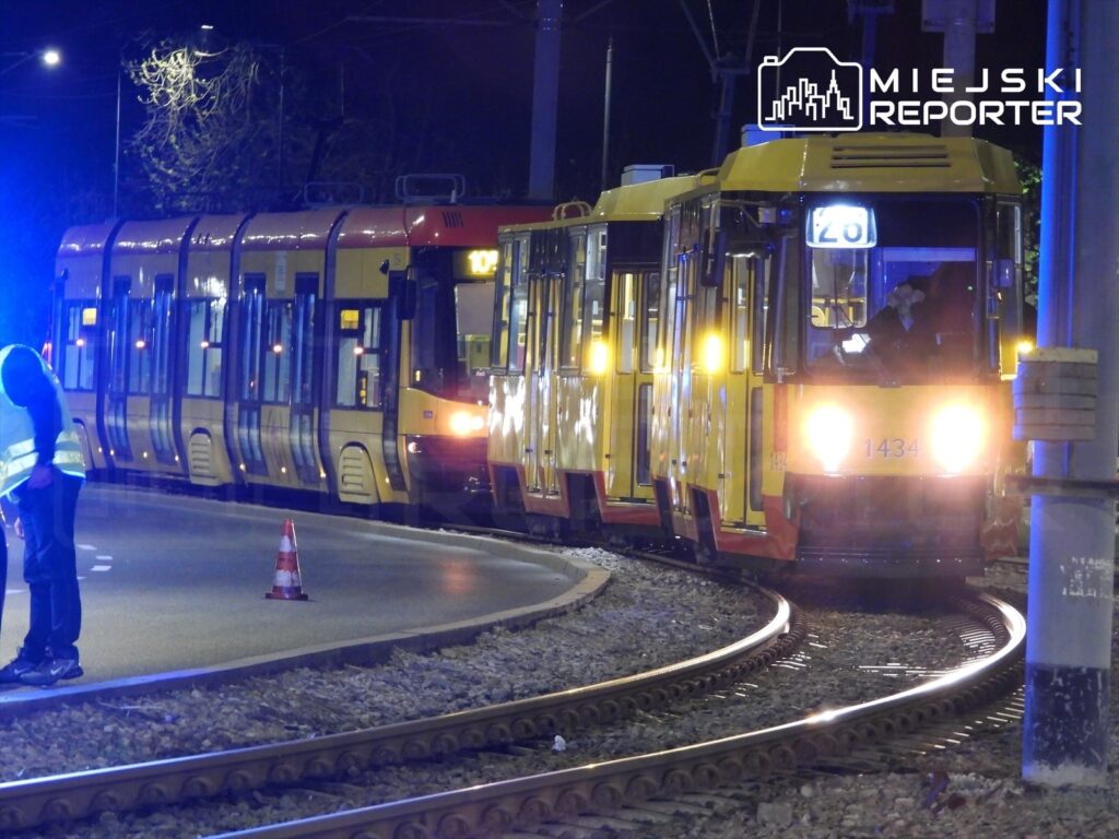 Tramwaje w nocy na skrzyżowaniu, przy jednym z nich mężczyzna w odblaskowej kamizelce sprawdza torowisko.