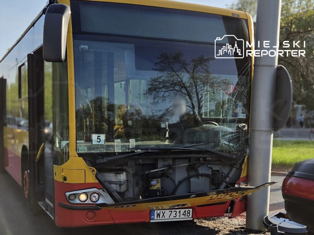 Autobus miejskiego transportu z uszkodzoną przednią częścią, zatrzymany przy słupie na ulicy.
