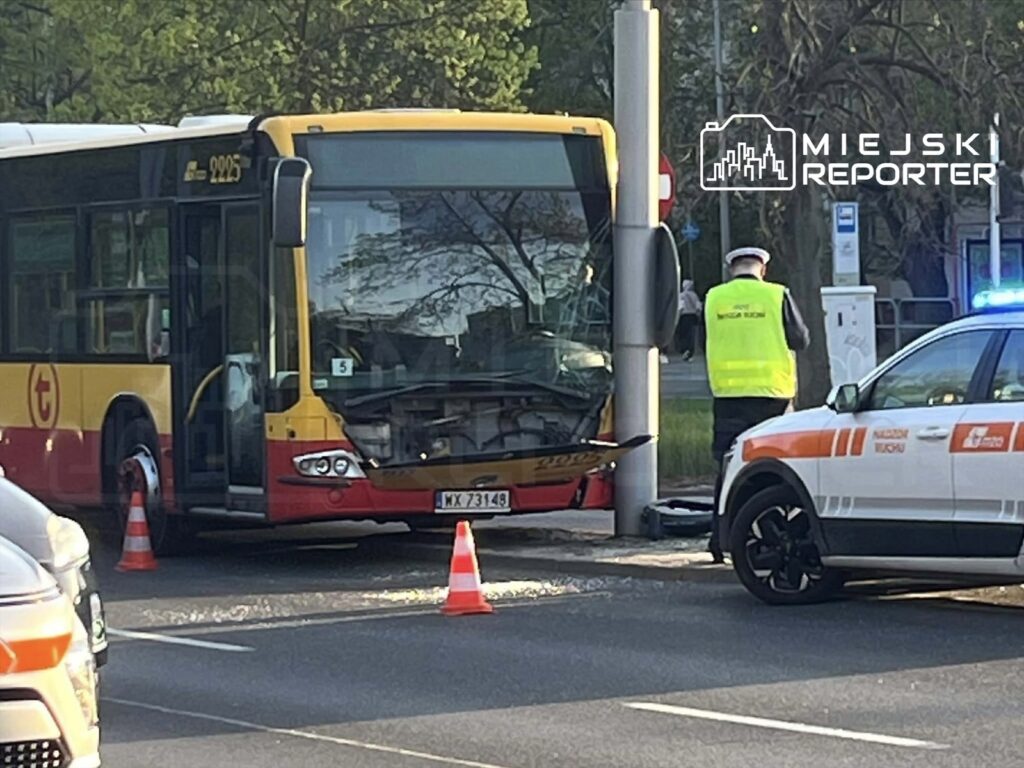 Autobus miejski z uszkodzonym przodem stoi na ulicy, obok niego policjant w kamizelce odblaskowej.
