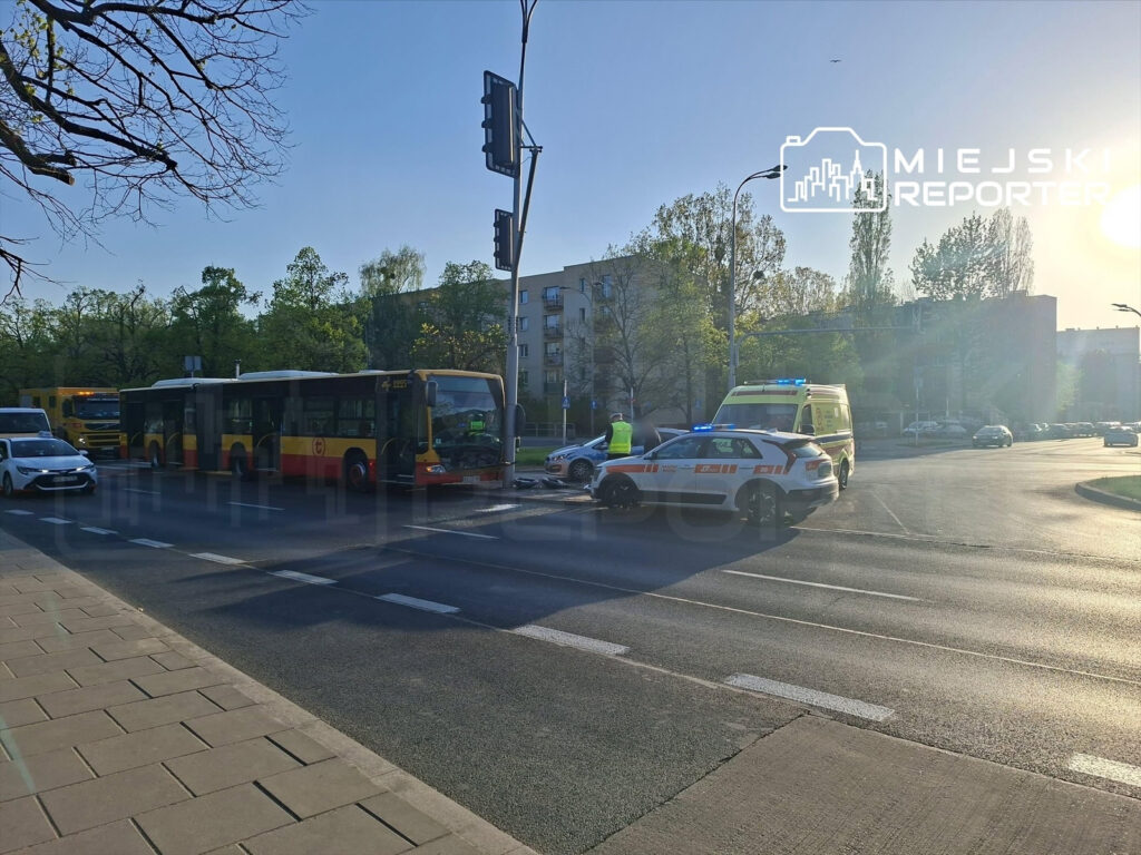 Kierowca autobusu zatrzymany na skrzyżowaniu, obok policyjny radiowóz i karetka, w tle budynki mieszkalne.