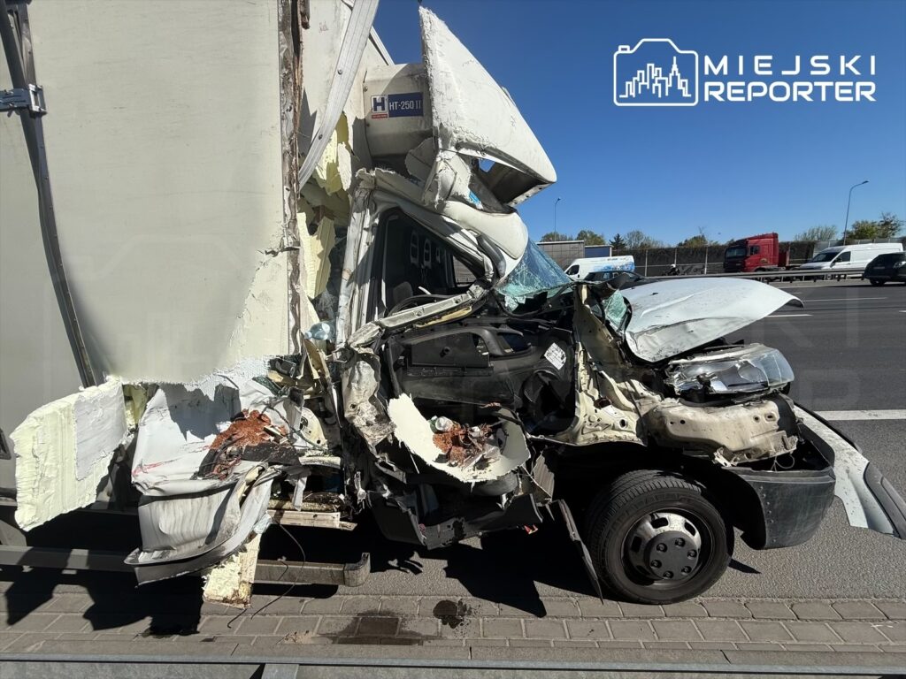 Zdeformowany samochód osobowy z uszkodzoną przednią częścią stoi obok ciężarówki na drodze.