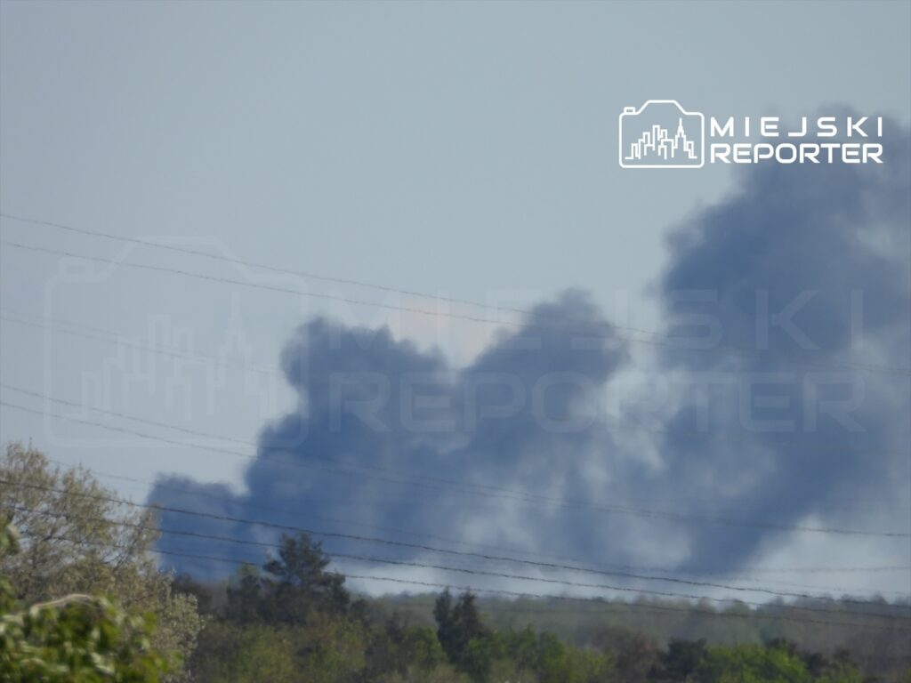 Czarny dym unoszący się w powietrzu nad zalesionym terenem w słoneczny dzień.