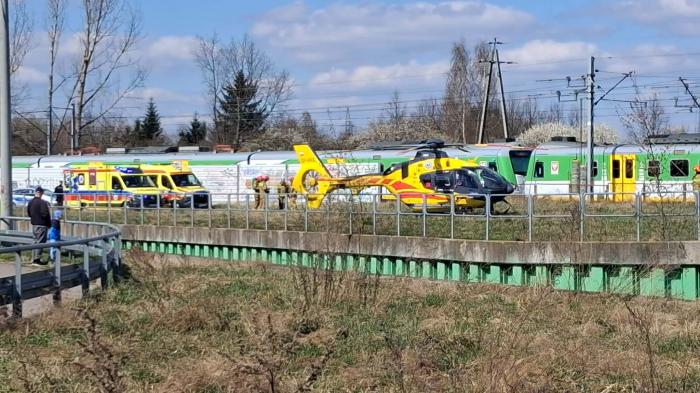 Na torach kolejowych lądowanie śmigłowca ratunkowego obok karetki pogotowia, w tle pociągi.