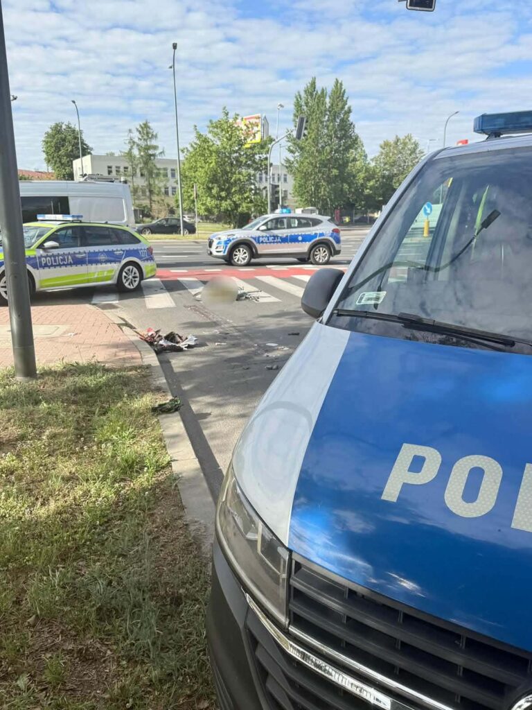 Policyjny radiowóz stoi na przejściu dla pieszych, obok widać drugi radiowóz oraz ślady zdarzenia na jezdni.