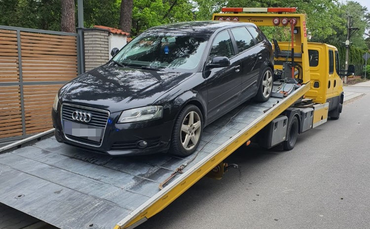 Czarny samochód marki Audi załadowywany na lawetę w miejskim otoczeniu.