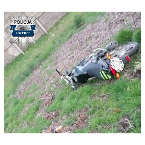 Motocykl leżący na boku na trawiastej powierzchni, w tle ogrodzenie.