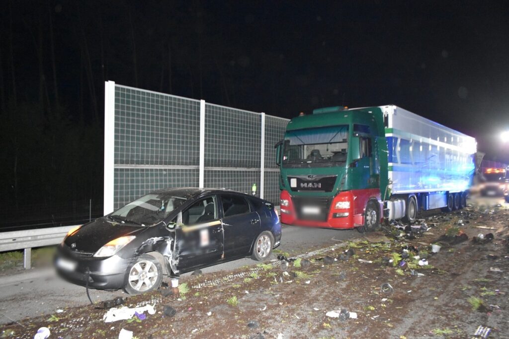 Zniszczony samochód osobowy stoi obok dużego ciężarowego pojazdu na drodze, otoczony odpadkami.
