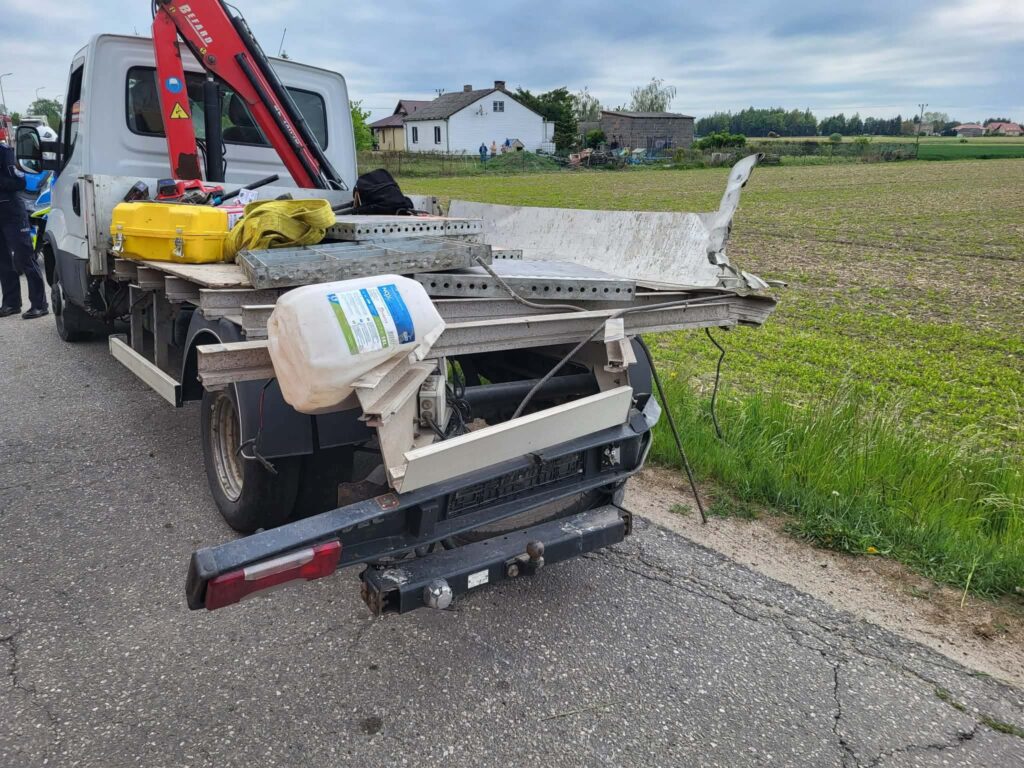 Samochód dostawczy z podniesioną platformą, obładowany narzędziami i materiałami, stoi na wiejskiej drodze.
