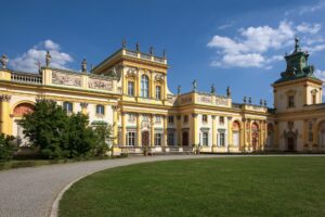 Wilanowski pałac z ozdobną fasadą i zielonym otoczeniem, pod jasnym niebem z białymi chmurami.