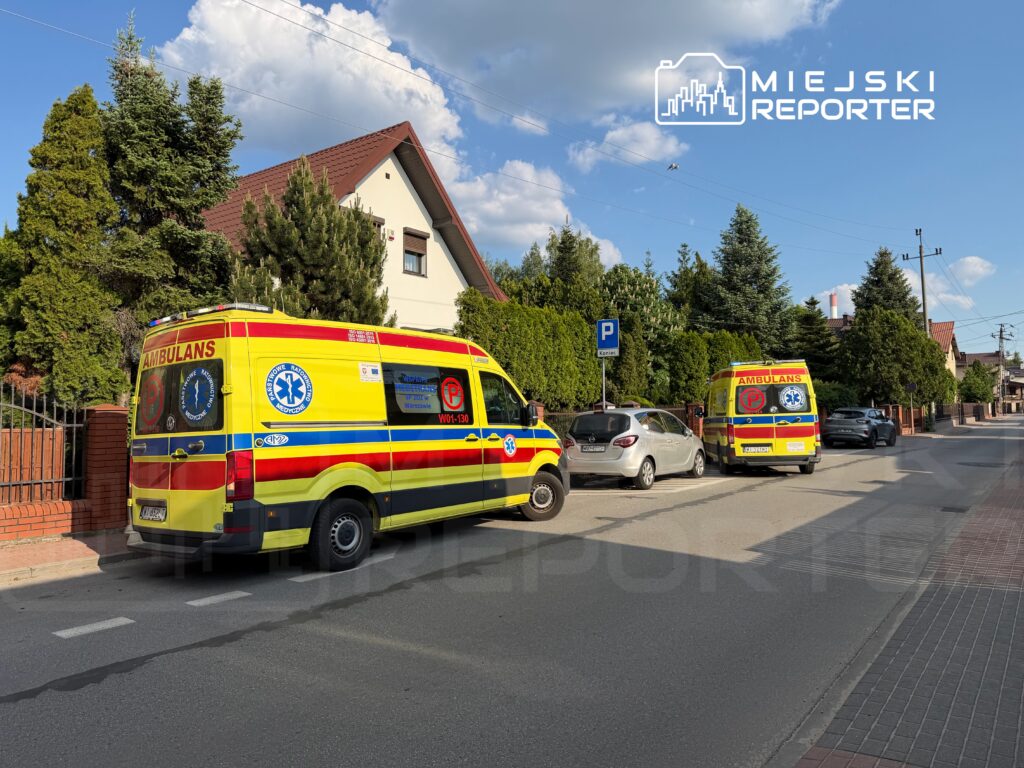 Dwa karetki pogotowia zaparkowane na ulicy w otoczeniu domów jednorodzinnych i drzew.