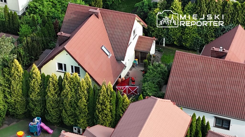 Widok na podwórko z domami, w tle zielone żywopłoty, a na pierwszym planie kolorowy plac zabaw z zjeżdżalnią.