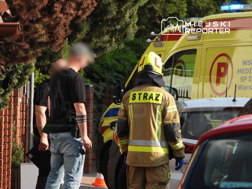 Mężczyzna w czarnej koszulce rozmawia z strażakiem w mundurze obok karetki pogotowia.