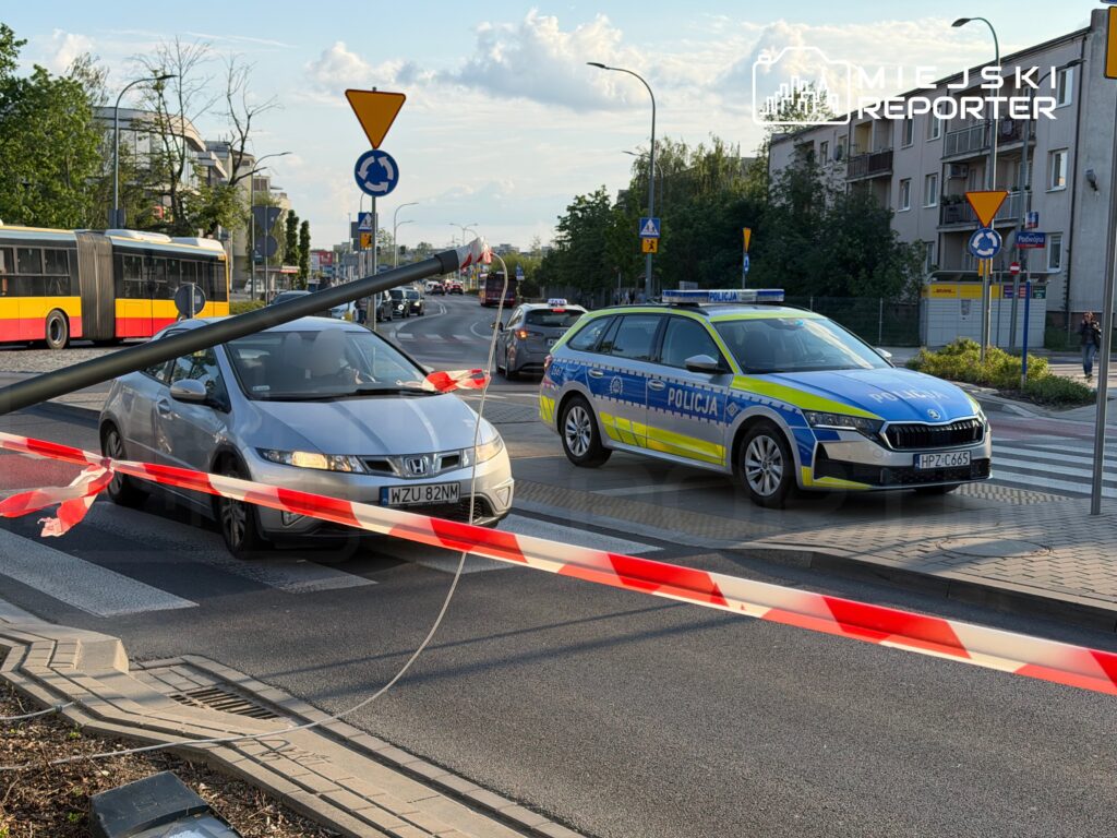 Samochód osobowy przejeżdża obok policyjnego radiowozu na drodze z barierką zabezpieczającą.