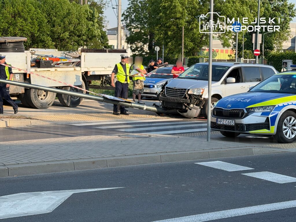 Policjanci w kamizelkach odblaskowych zabezpieczają miejsce kolizji, gdzie samochód uderzył w latarnię.