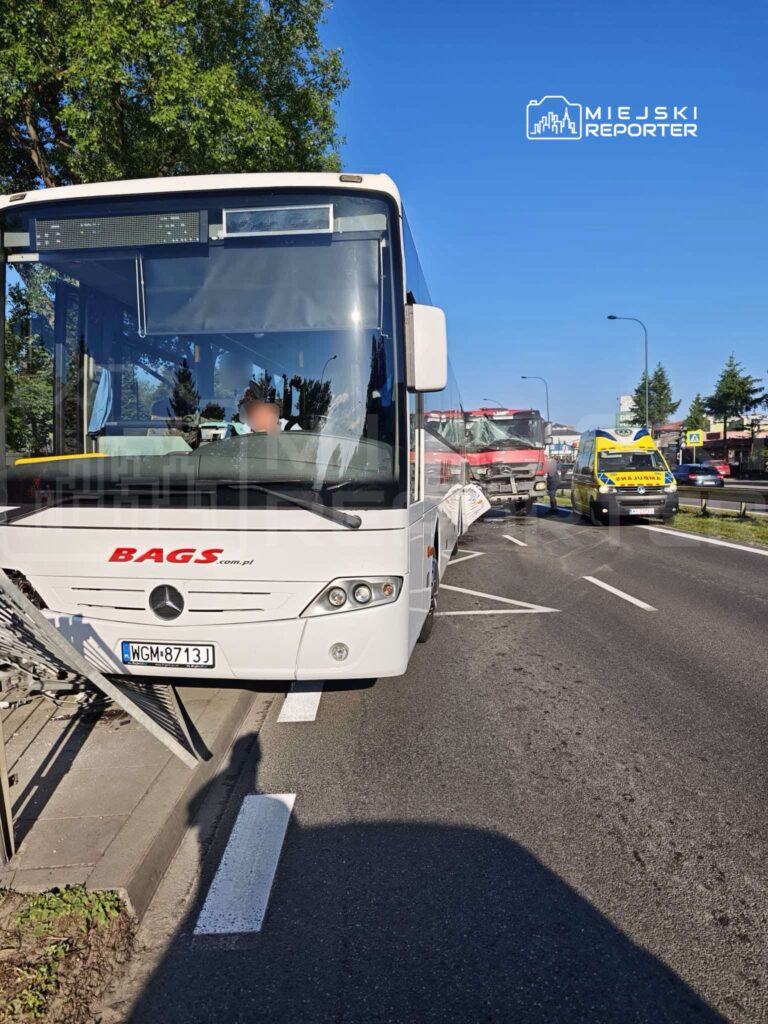 Autobus turystyczny zatrzymany na drodze, obok uszkodzony pojazd ciężarowy oraz karetka pogotowia.