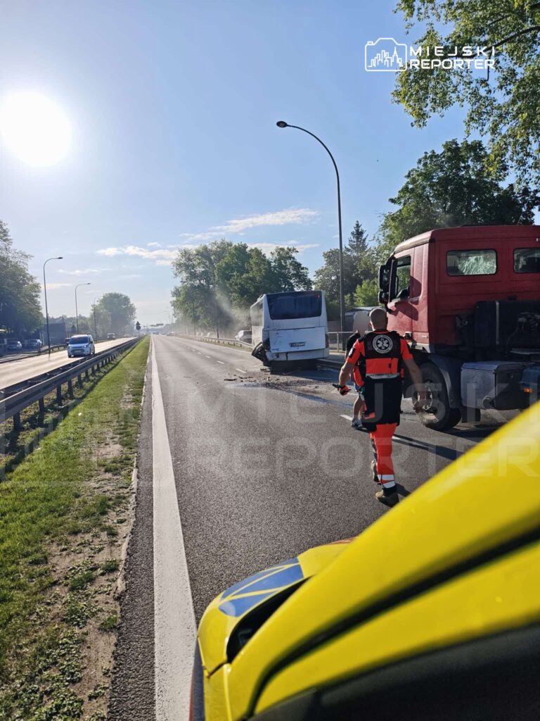 Ratownik w pomarańczowym uniformie podchodzi do uszkodzonego autobusu na drodze, obok przejeżdżające samochody.