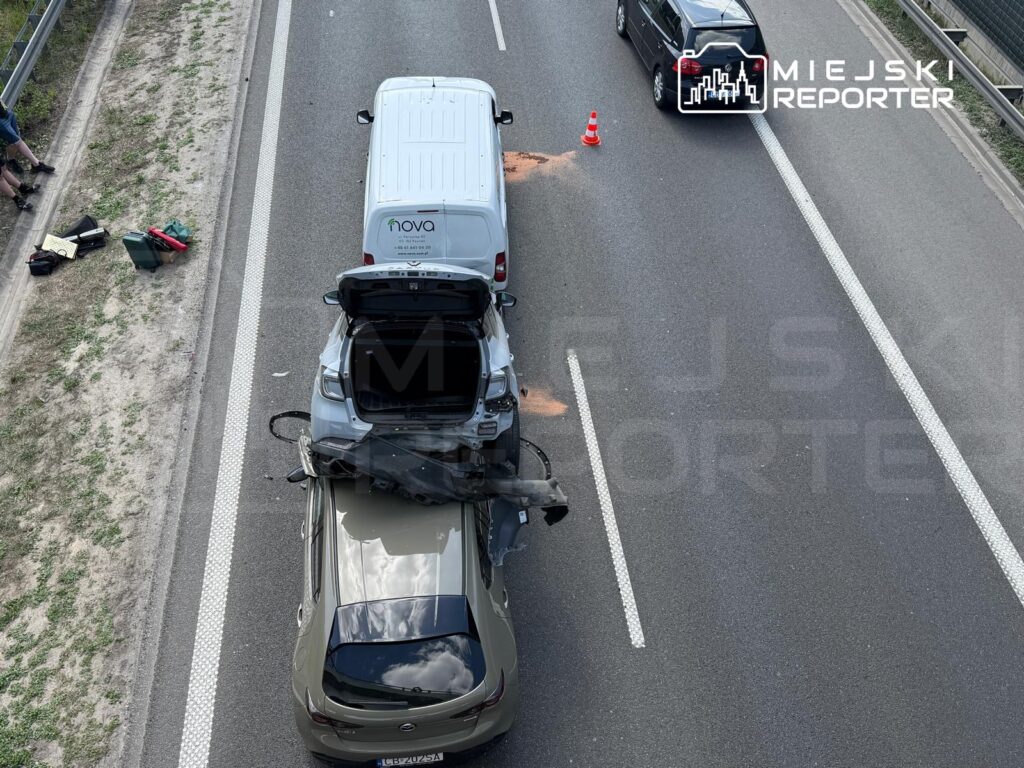 Wielki wypadek drogowy z udziałem dwóch samochodów na jezdni, z porzuconymi przedmiotami na poboczu.