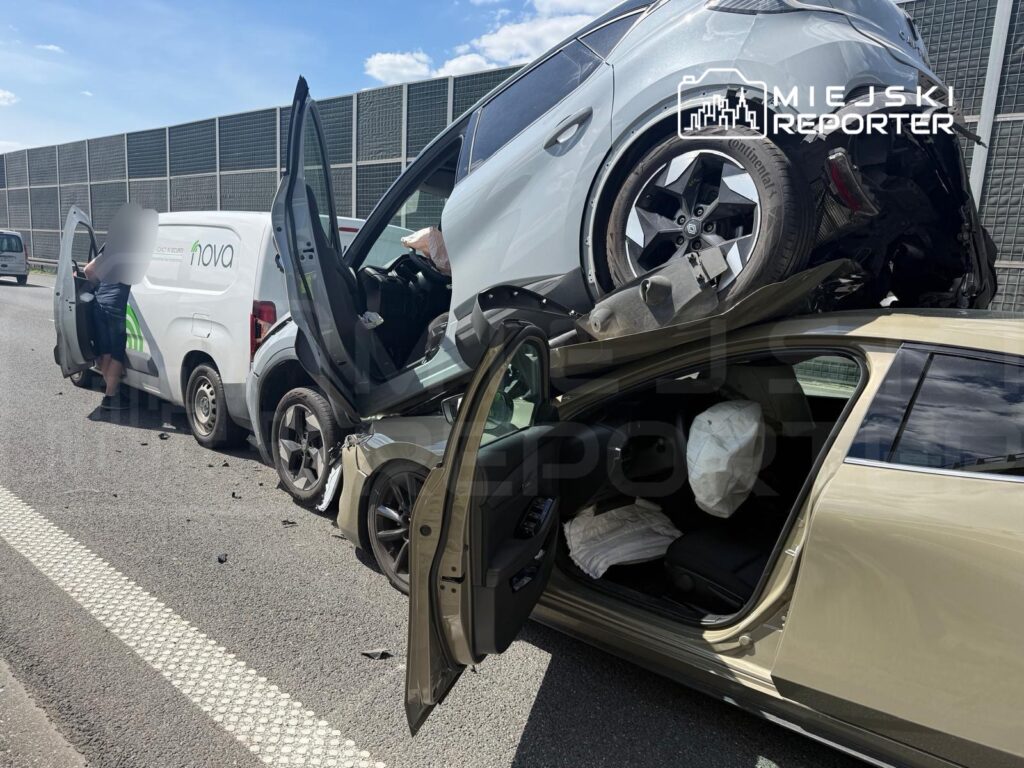 Wielokrotny wypadek drogowy, w którym samochód osobowy leży na dachu innego pojazdu, a obok stoi furgonetka.