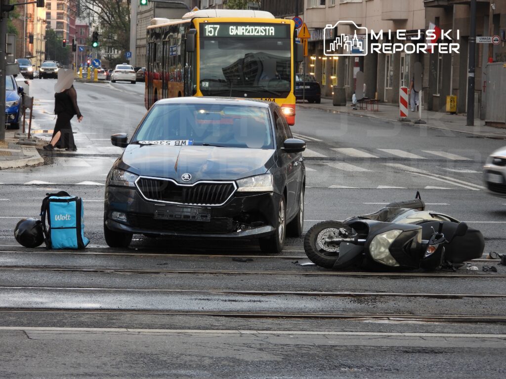 Czarny samochód osobowy stoi na torowisku obok przewróconego motocykla, obok leży torba dostawcza.