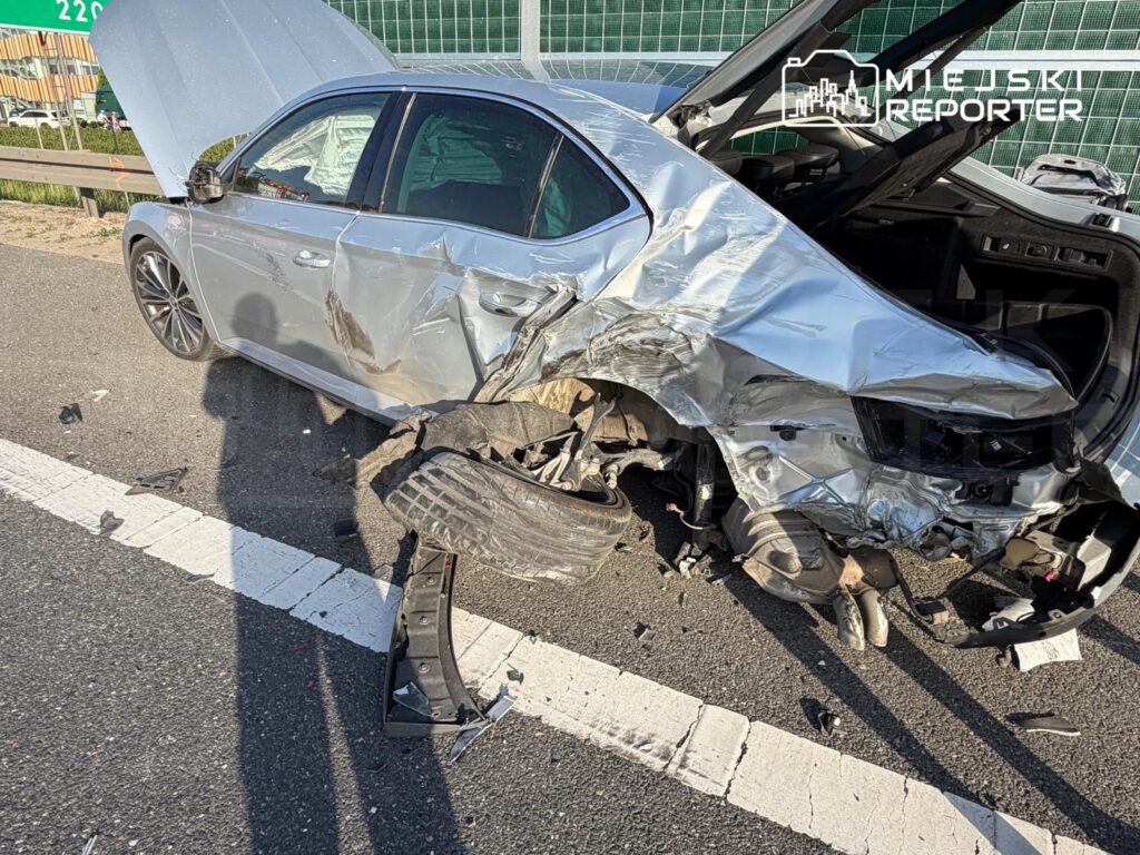Uszkodzone auto osobowe z wgniecioną tylną częścią stoi na poboczu drogi, obok leżą fragmenty karoserii.