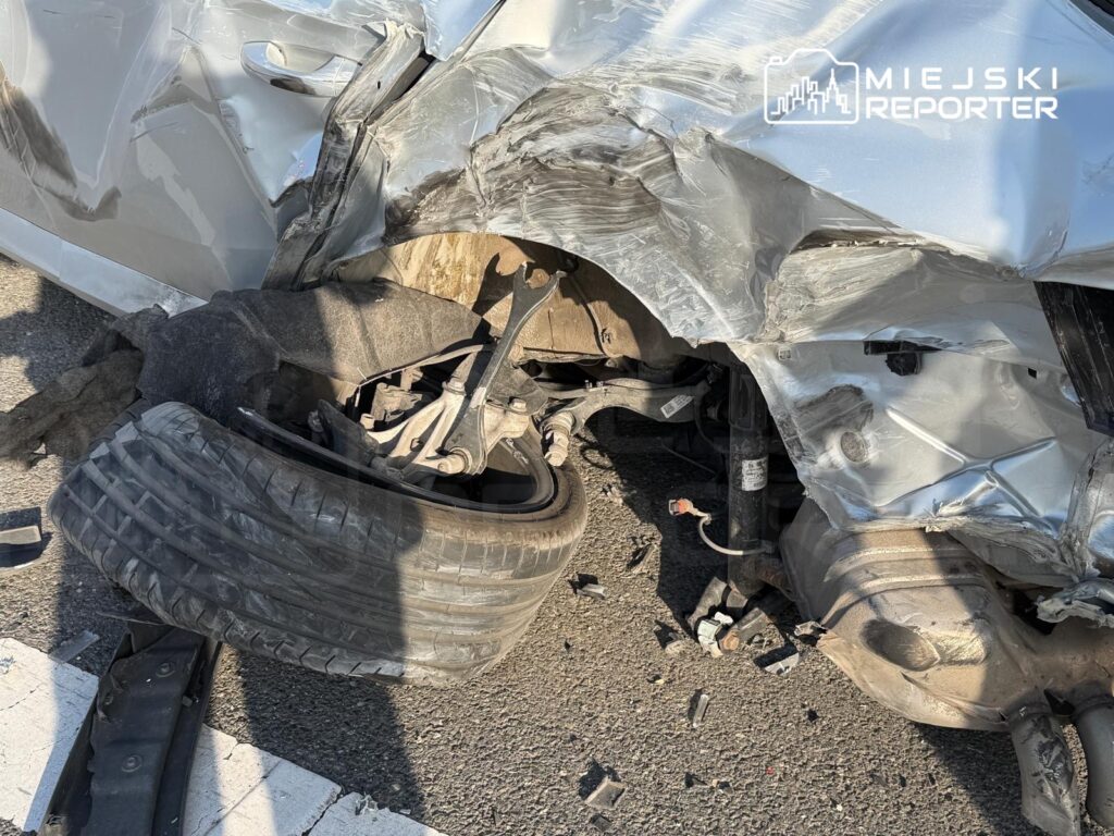Uszkodzony samochód z zniekształconą karoserią i oderwaną oponą leży na jezdni, otoczony odłamkami.