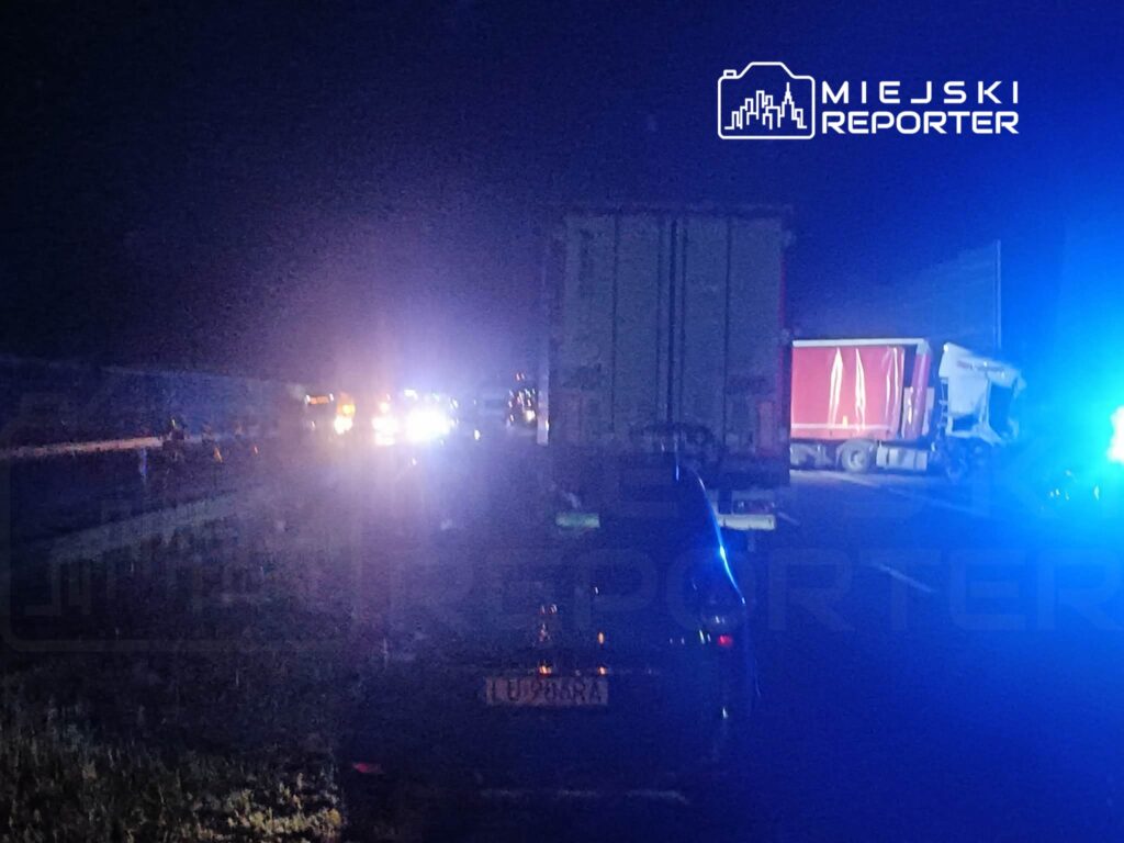 Na drodze nocą widać pojazdy ratunkowe oraz ciężarówki, z których jedna jest uszkodzona.