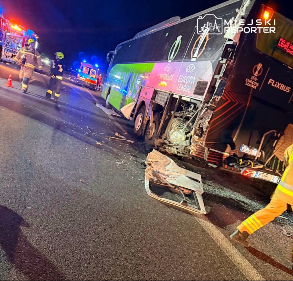W nocy strażacy i ratownicy medyczni pracują przy uszkodzonym autobusie, na drodze z widocznymi śladami wypadku.