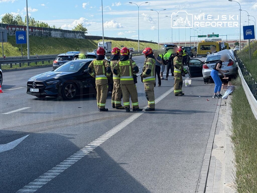 Grupa strażaków udziela pomocy po wypadku drogowym na autostradzie, obok uszkodzonego samochodu osobowego.