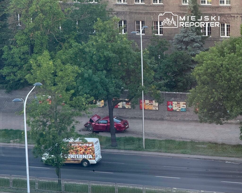 Czerwony samochód zaparkowany z otwartą klapą bagażnika obok chodnika, obok przejeżdżająca ciężarówka z napisem "Cukiernia".