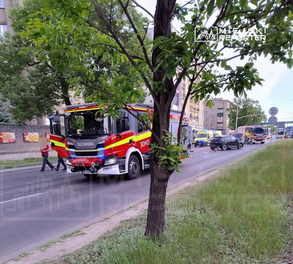 Strażacy przy samochodzie gaśniczym na drodze, obok widać uszkodzony pojazd oraz inne służby ratunkowe.