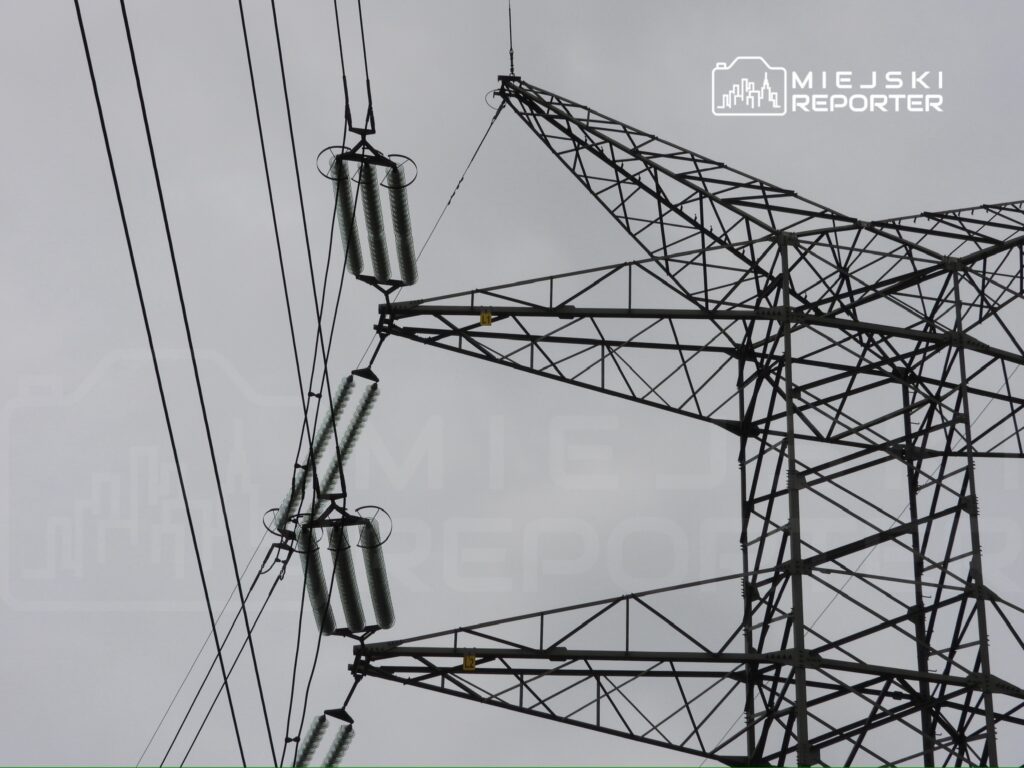 Wysoka wieża energetyczna z przewodami elektrycznymi na tle szarego nieba.