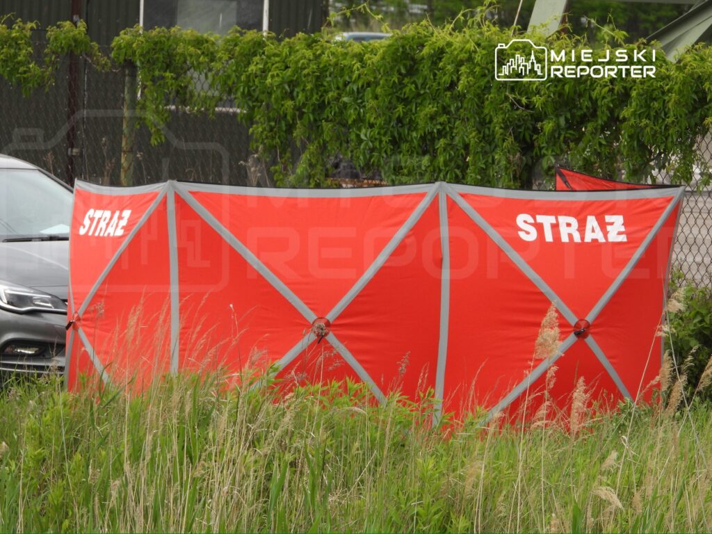 Czerwony namiot z napisem "STRAŻ" ustawiony w trawie obok zaparkowanego samochodu.