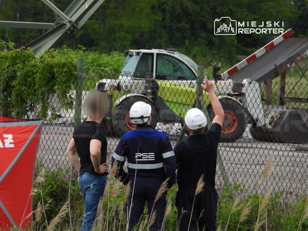 Trzech mężczyzn, w tym jeden w hełmie, obserwuje ciężki pojazd z podnoszoną skrzynią na placu budowy.