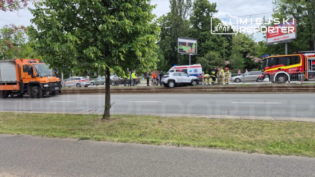 Wielu ratowników i strażaków pracuje przy uszkodzonym samochodzie na torach tramwajowych.