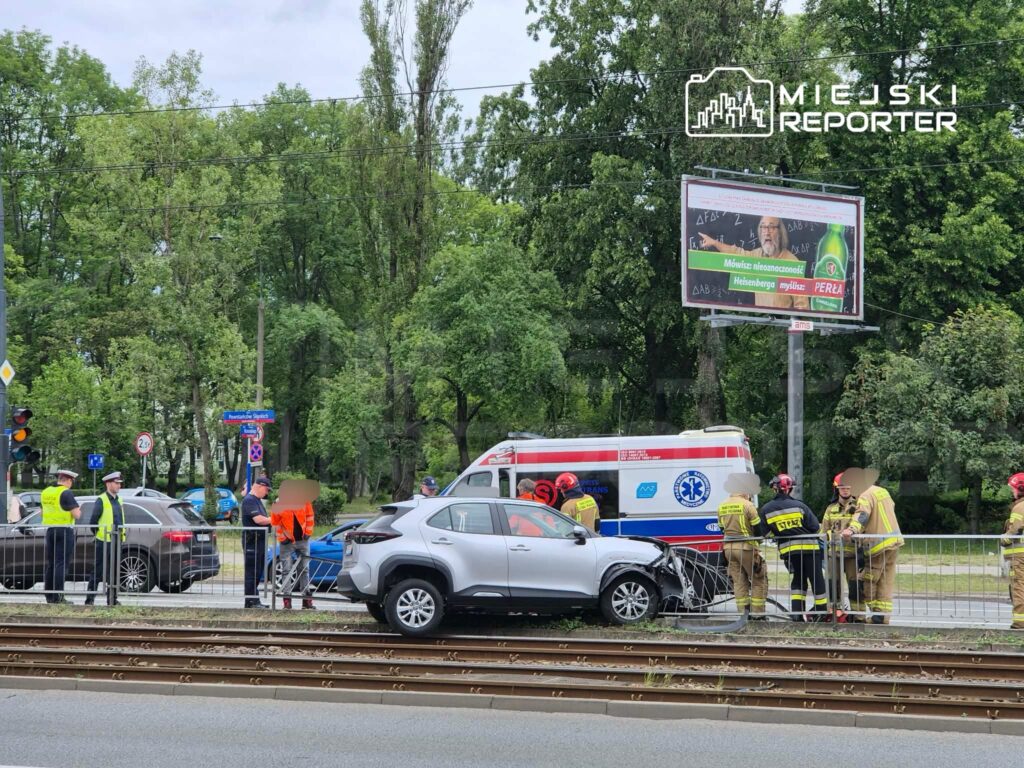Wielu funkcjonariuszy policji i straży pożarnej zabezpiecza miejsce wypadku drogowego przy torach tramwajowych.