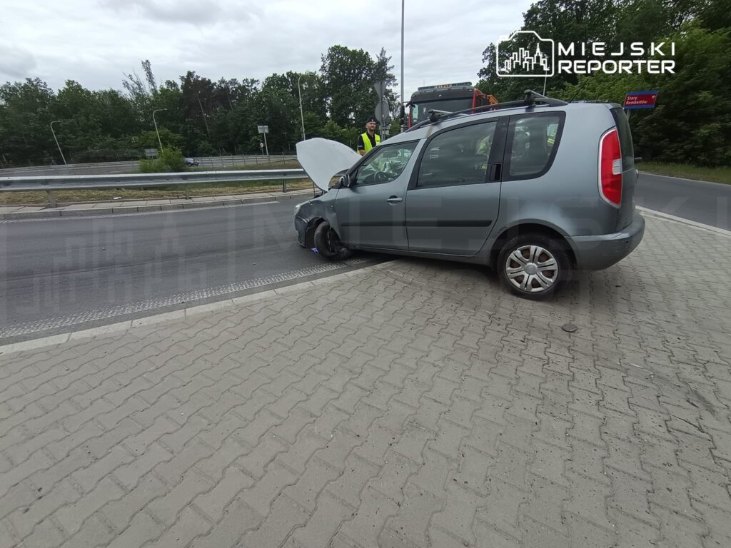 Zepsuty samochód osobowy z otwartą maską zaparkowany na poboczu drogi, obok stoją pracownicy pomocy drogowej.