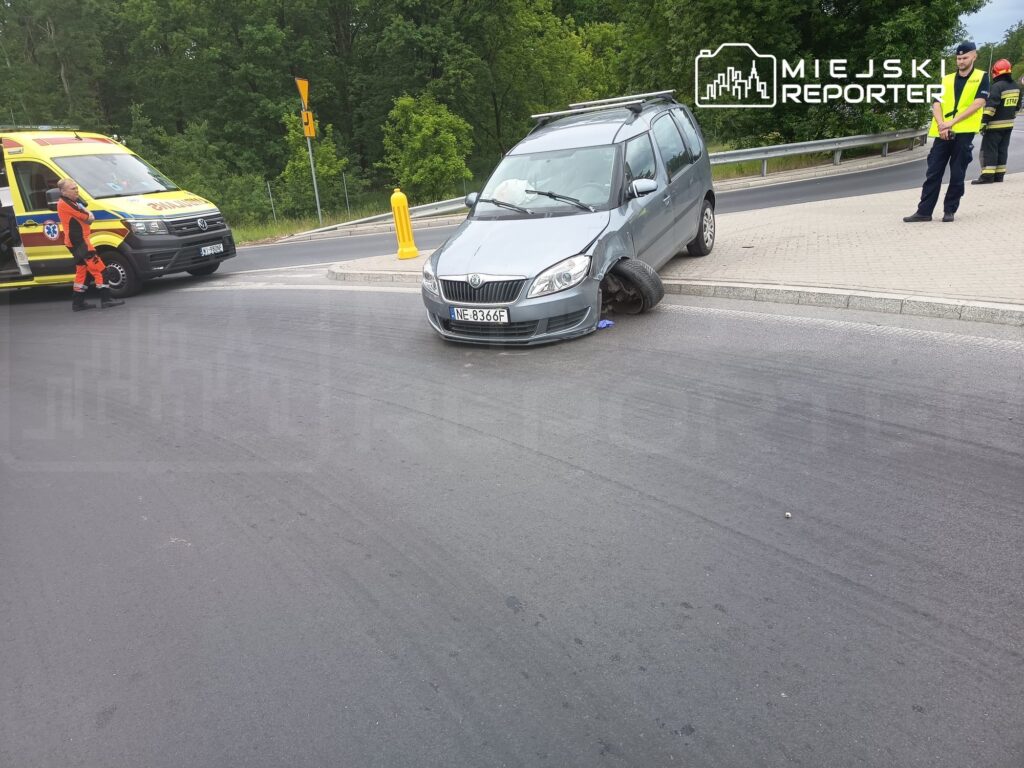 Samochód osobowy z uszkodzoną oponą stoi na poboczu drogi, obok niego zespół ratunkowy w akcji.