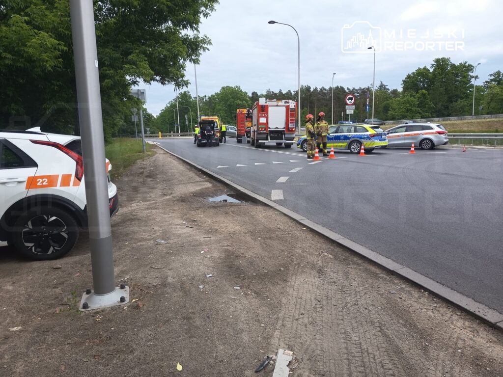 Na drodze odbywa się akcja ratunkowa, w której biorą udział strażacy oraz pojazdy służb ratunkowych.
