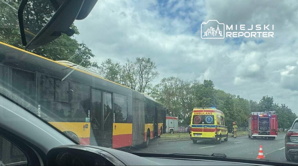 Wielki autobus stoi na poboczu, obok niego karetka i wóz strażacki, a strażacy prowadzą działania ratunkowe.
