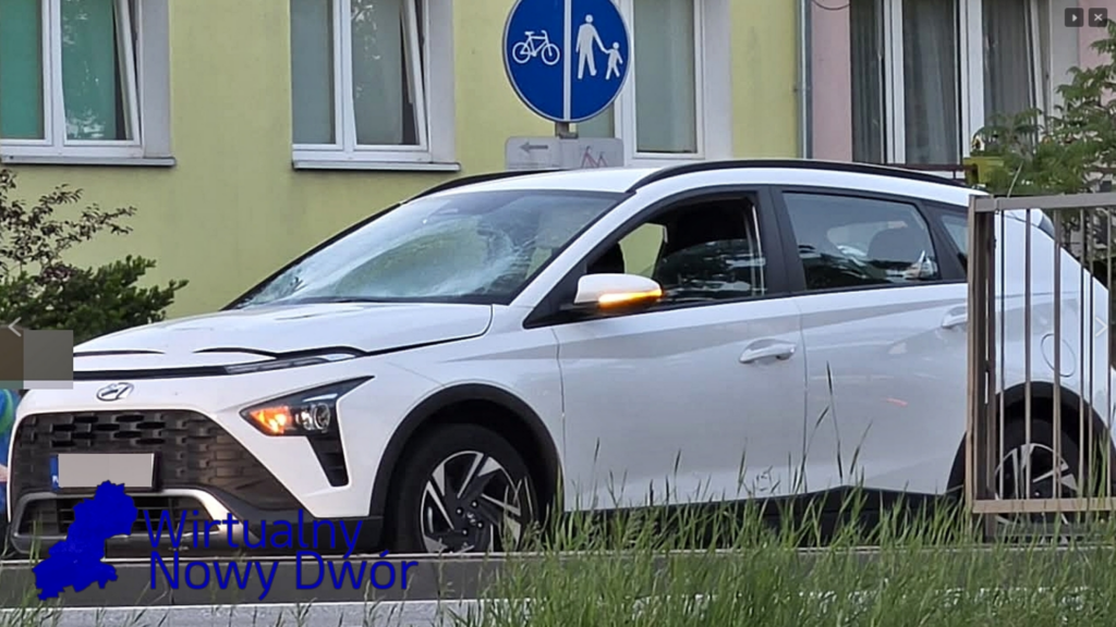 Biały samochód osobowy zaparkowany obok znaku drogowym dla pieszych i rowerów w miejskim otoczeniu.