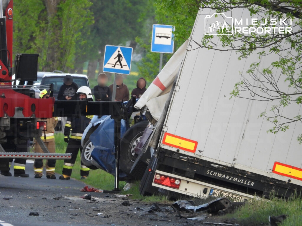 W miejscu wypadku drogowego ratownicy i strażacy pracują przy przewróconym samochodzie osobowym oraz ciężarówce.