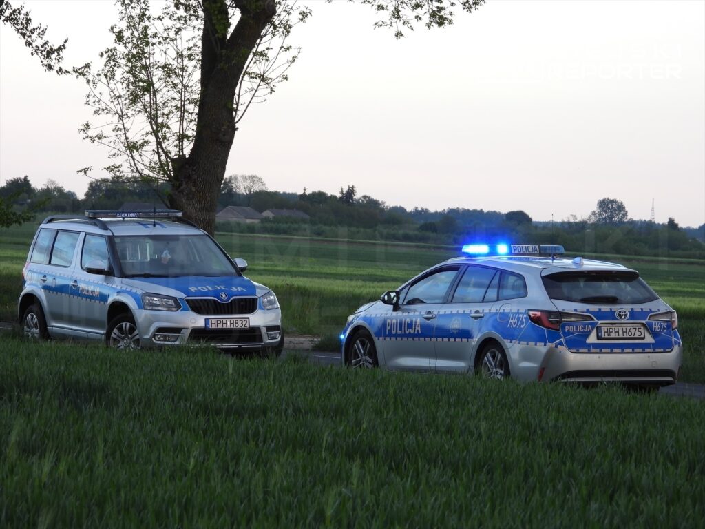 Dwa radiowozy policyjne zaparkowane w polu, jeden z włączonymi sygnalizatorami świetlnymi.