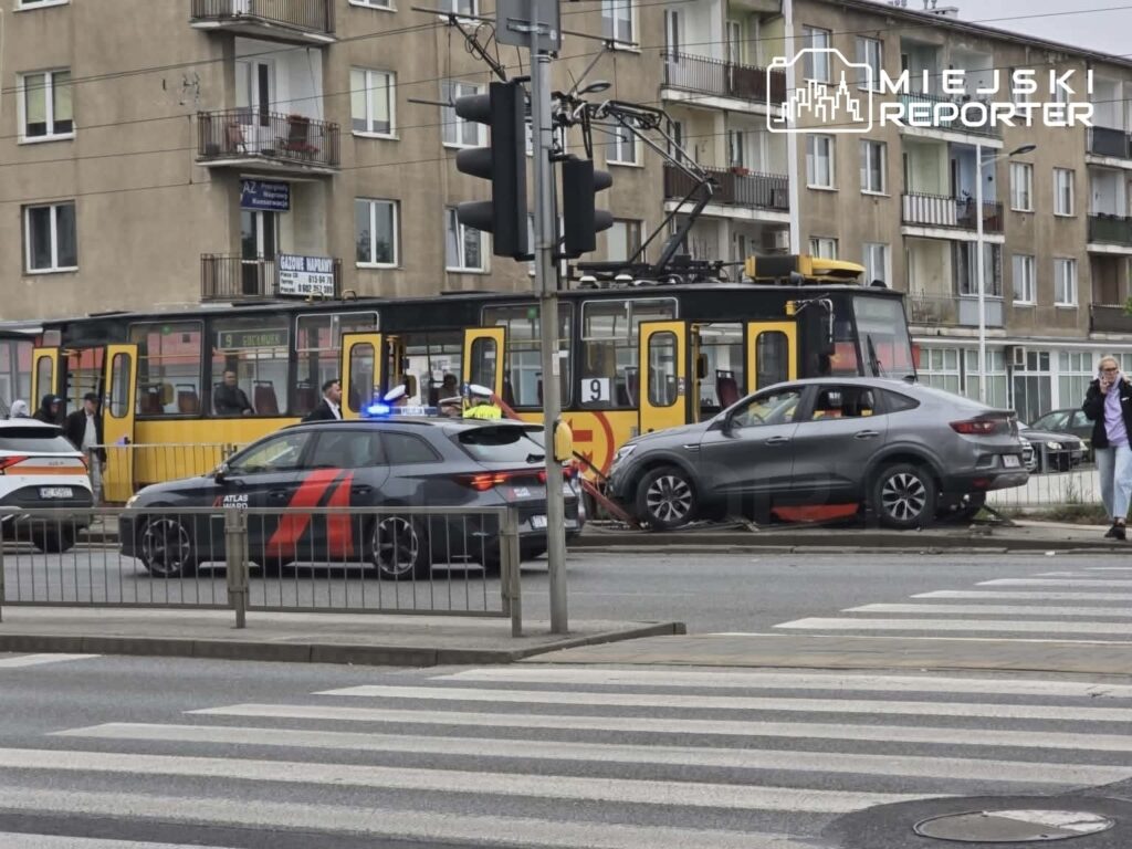 Zderzenie tramwaju z samochodem osobowym na skrzyżowaniu, obok policyjne radiowozy i przechodnie.